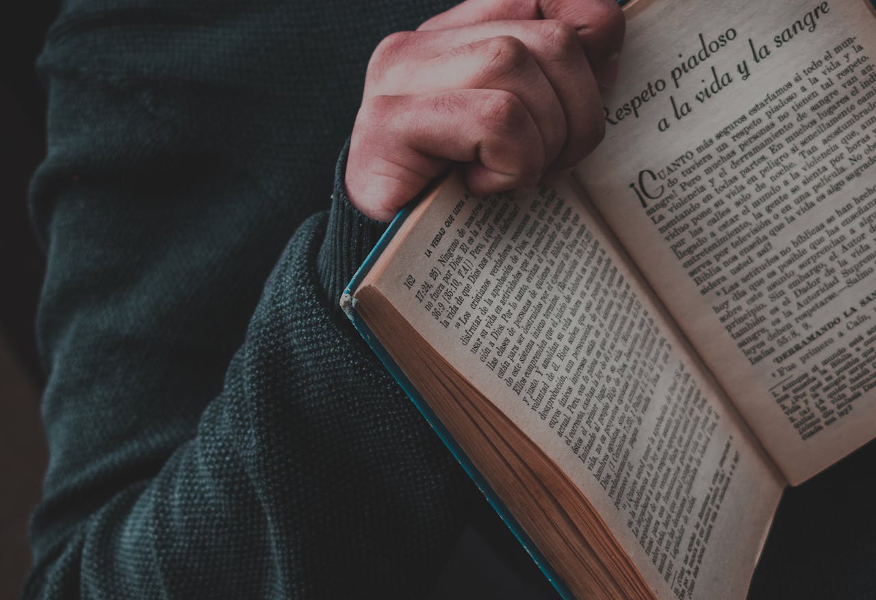 A close-up view of a hand holding an open Spanish book, showcasing text on pages.