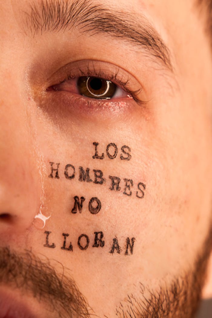 Emotional close-up of a mans eye with tear and tattooed message.
